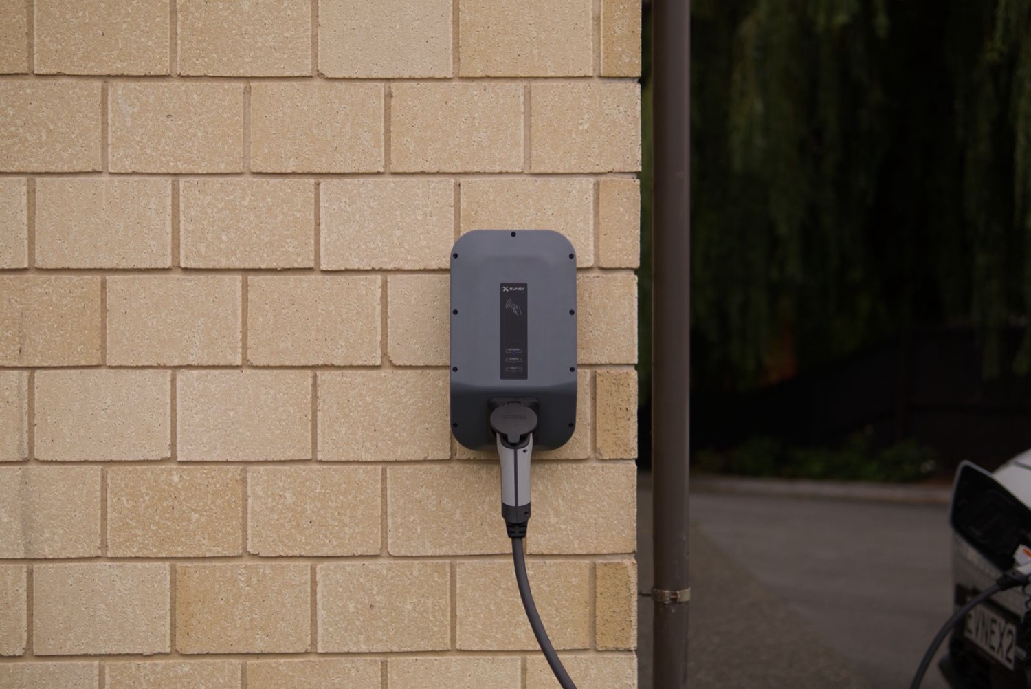 A home EV charger mounted on a house wall above a quiet driveway