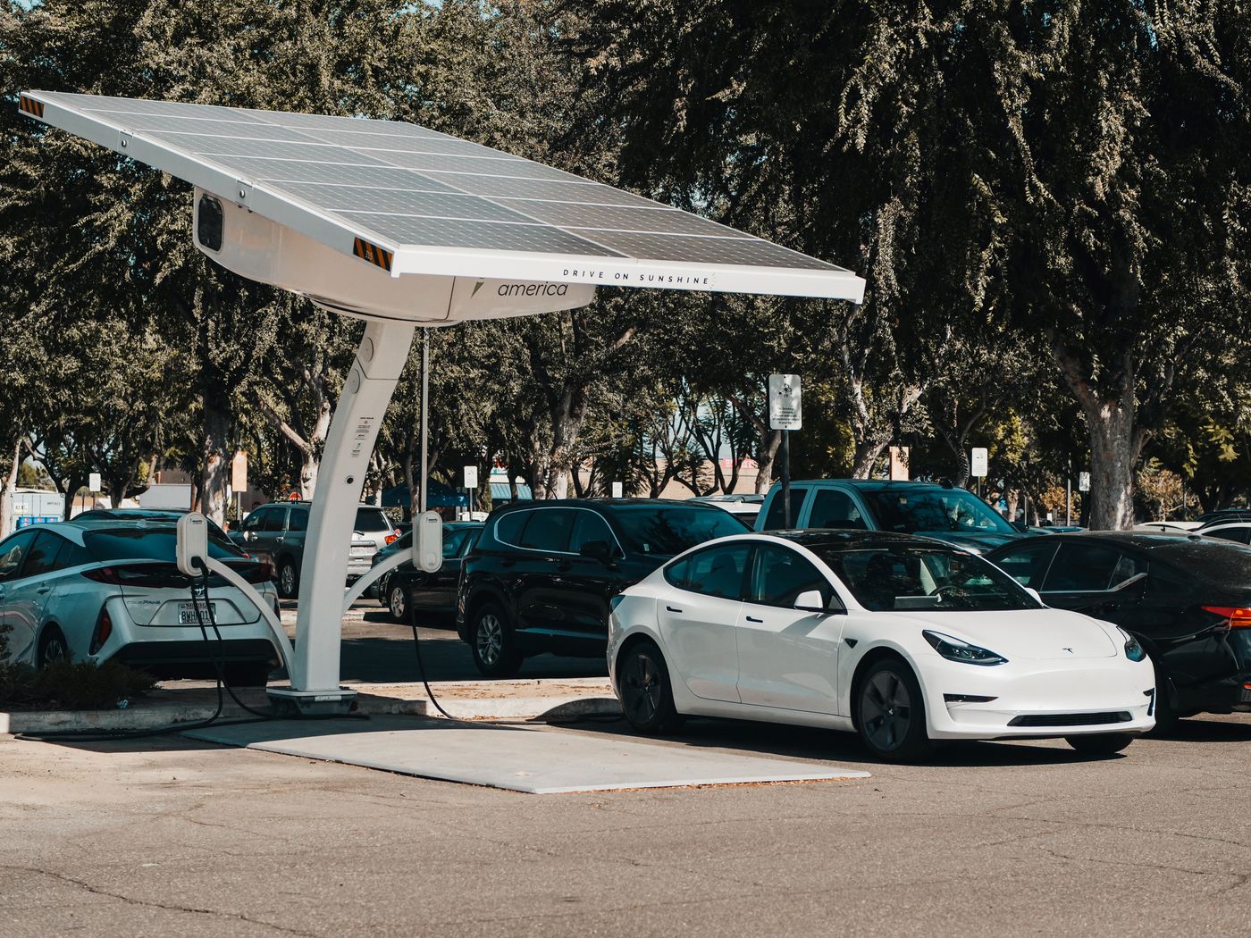A public EV charging station in a busy car park, cars parked all around it